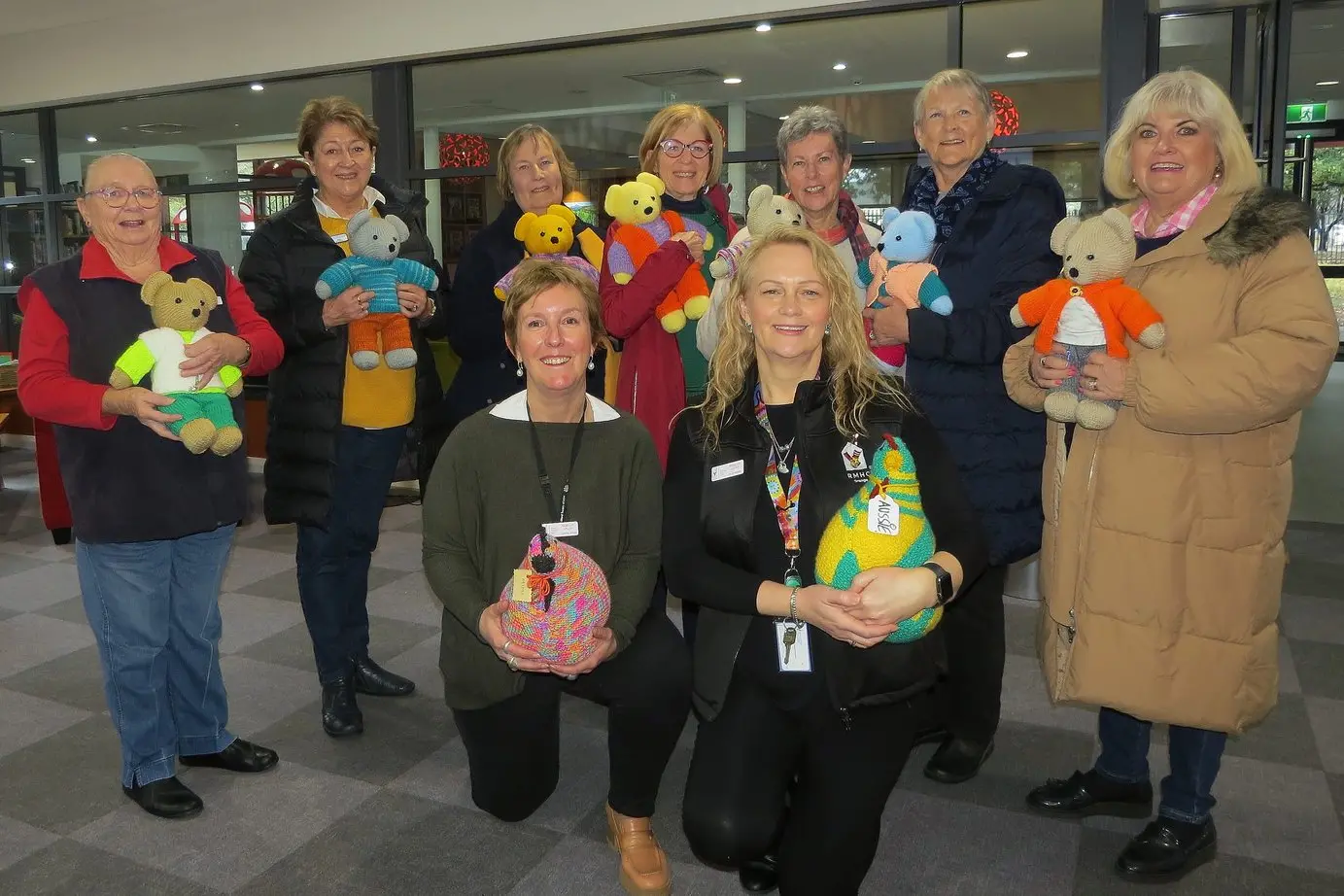 Cowra Evening CWA members Cheryl McAlister, Ann Apthorpe, Ros Ryan, Kaye Kilby, Kay Best, Helen Findlay and Wendy Dick, each holding a teddy knitted by Shirley Flint of Cowra with RMHCW staff Rebecca and Bronwyn holding donated knitted chickens.